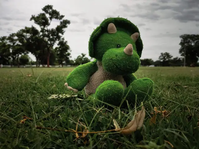 A green plush triceratops sitting on grass in a park