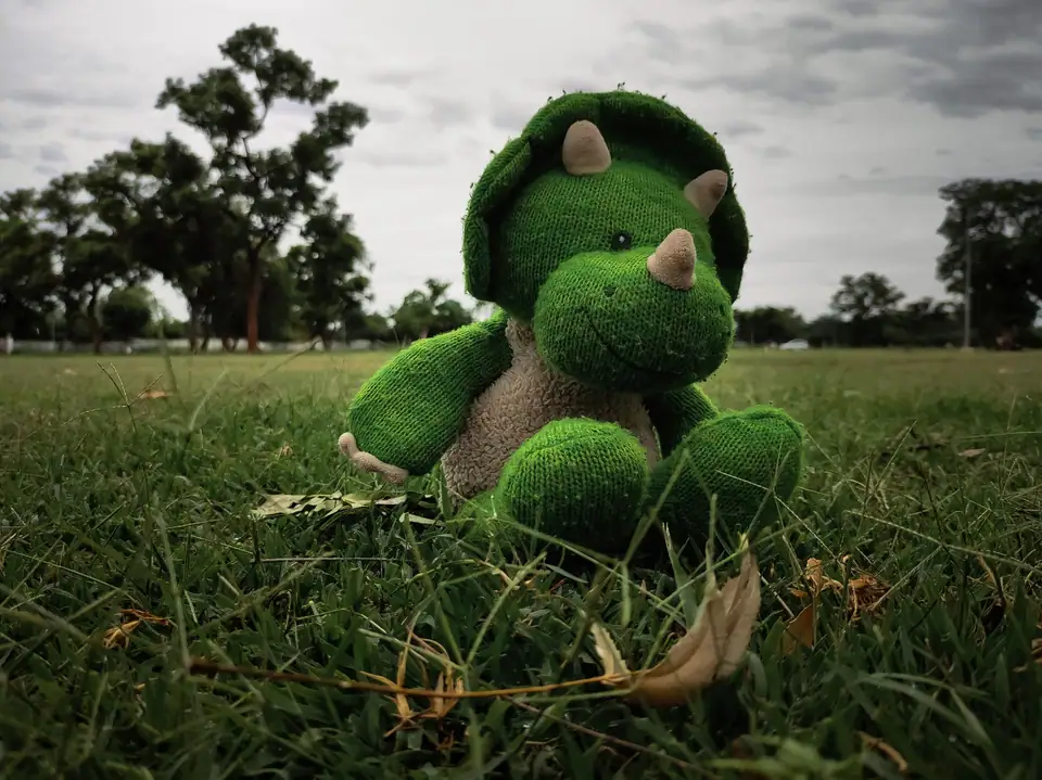 A green plush triceratops sitting on grass in a park