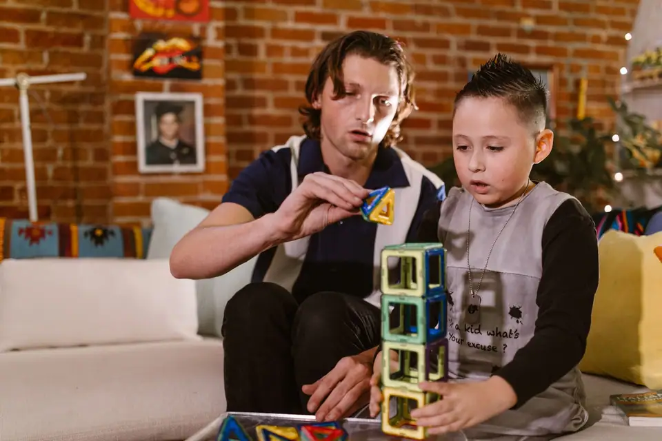 A boy and a man stacking colorful see-through magnetic tiles into a tower on a living room table